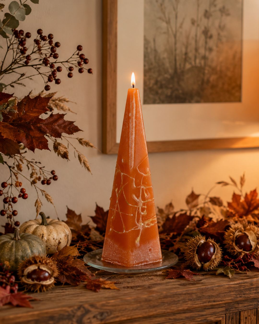 Orange pyramidenförmige Designkerze mit Herbstdekoration auf rustikalem Sideboard