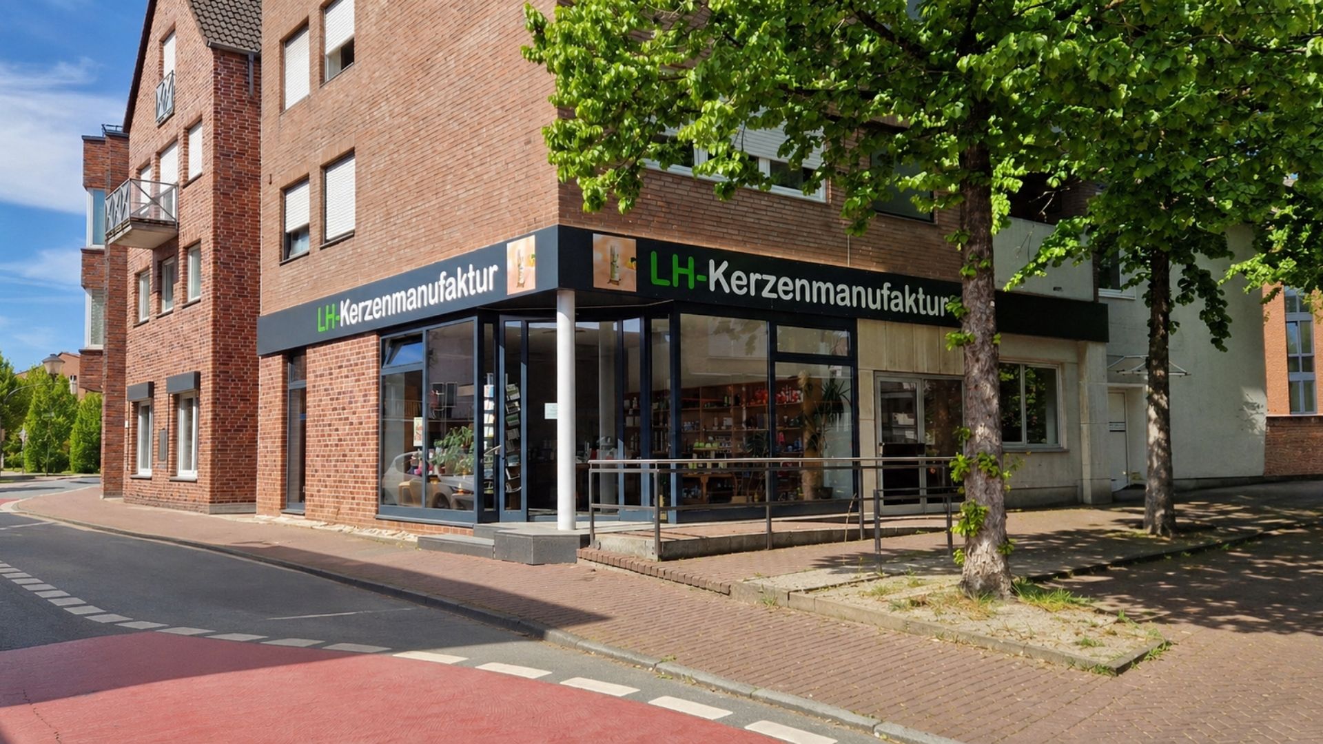 Außenansicht der LH-Kerzenmanufaktur Straßenansicht der LH-Kerzenmanufaktur mit beschriftetem Ladeneingang und Schaufenstern