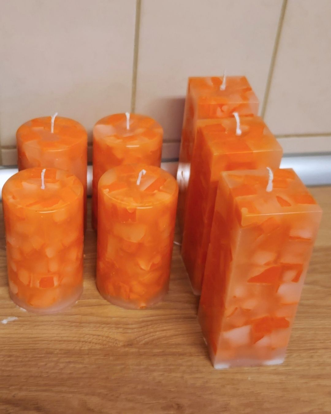 Orange Mosaikkerzen nach dem Entformen Mehrere orange Mosaikkerzen mit weißen Dochten stehen nach dem Entformen auf einer Holzfläche.