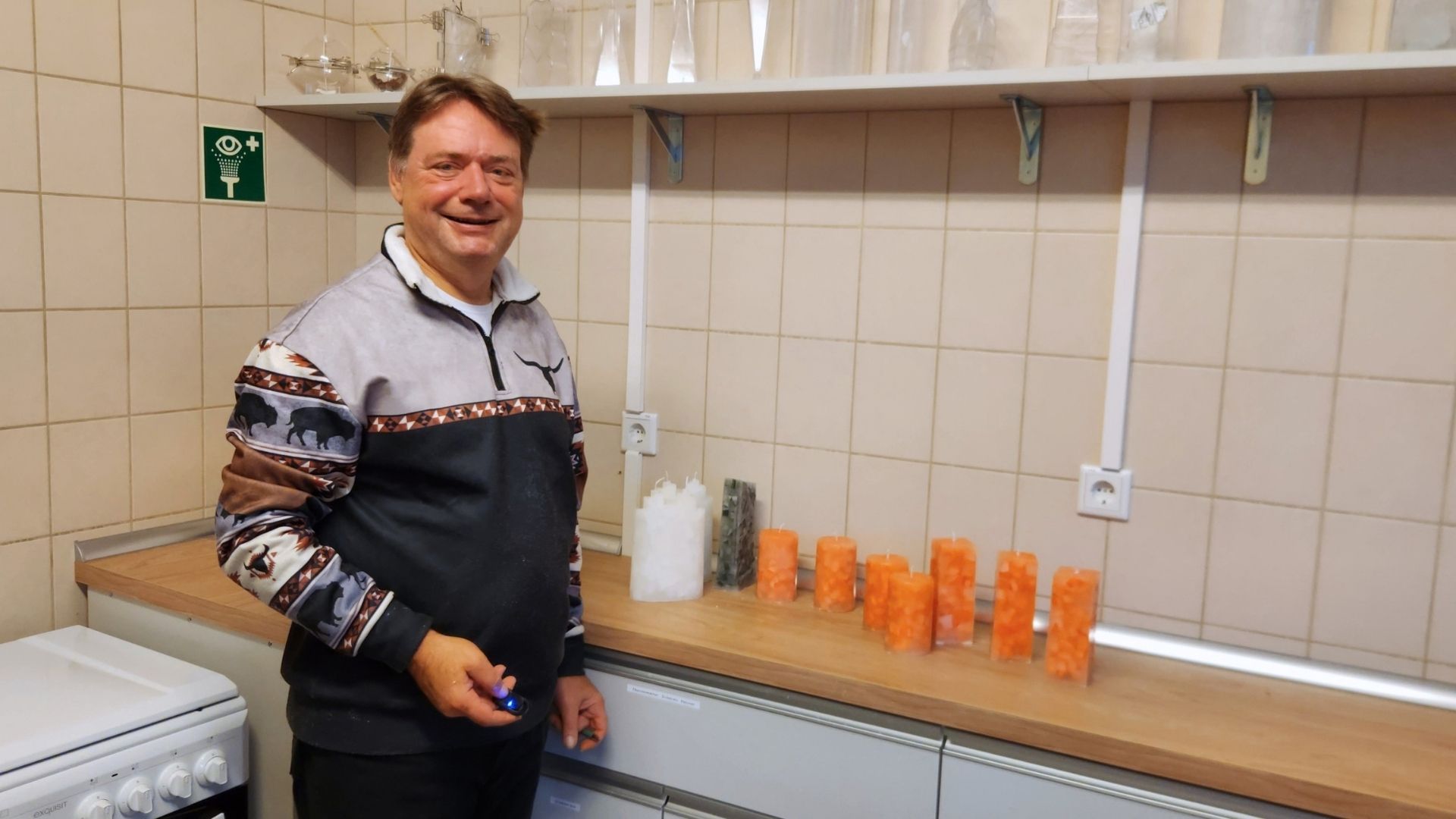 Mann steht in der Kerzengießerei neben orangefarbenen Mosaikkerzen und maßgefertigten Arbeitsflächen