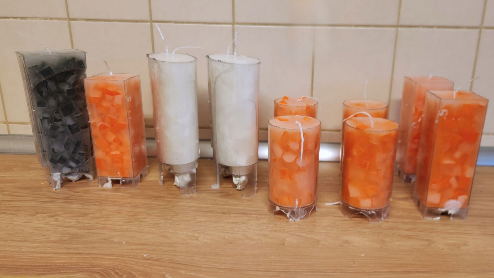 Orange und weiße Mosaikkerzen mit Dochten stehen vor dem Entformen in transparenten Gießformen.