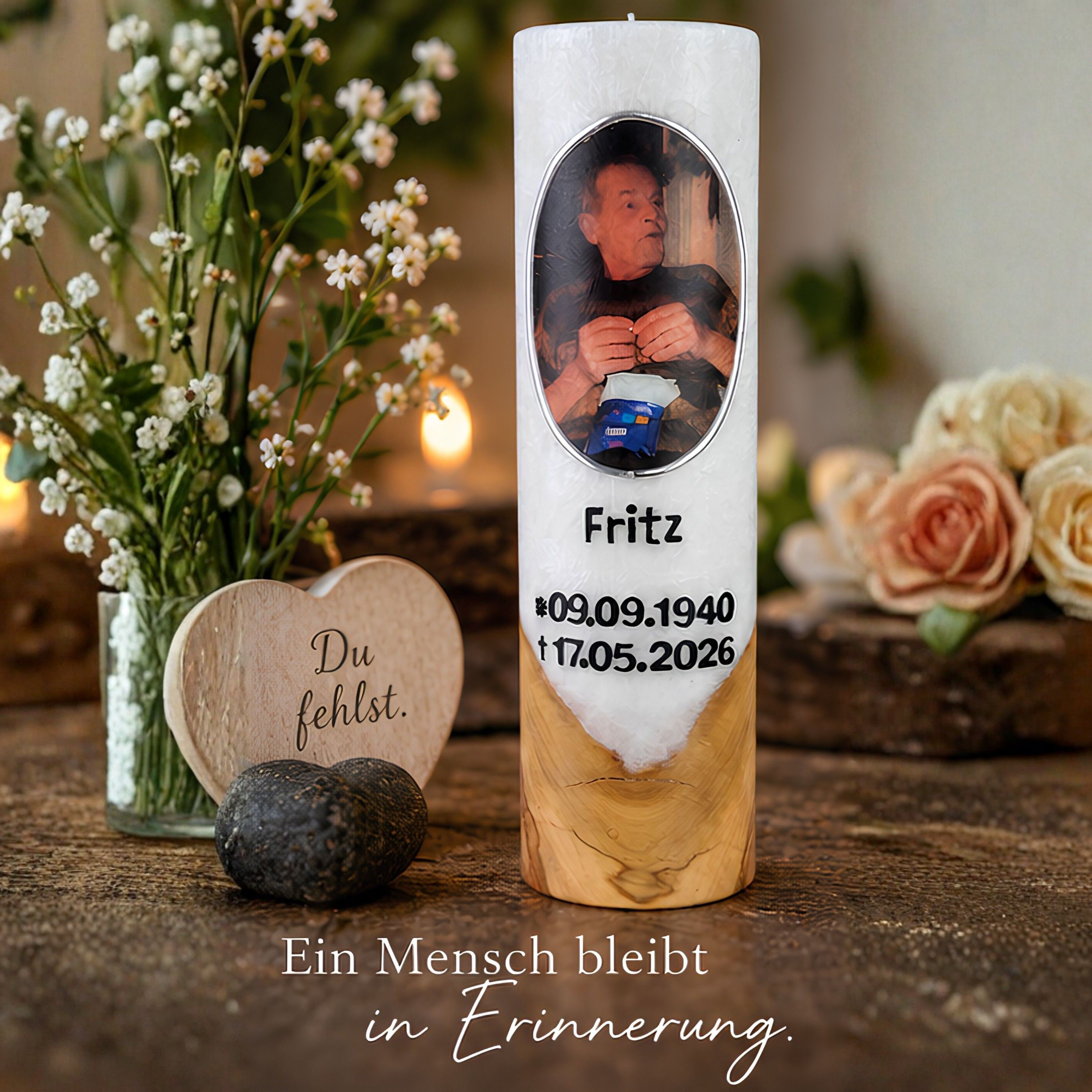 Personalisierte Trauerkerze mit Foto Weiße Holzkerze mit Foto, dem Namen Fritz und erhabenen Lebensdaten neben Blumen und Gedenkdekoration