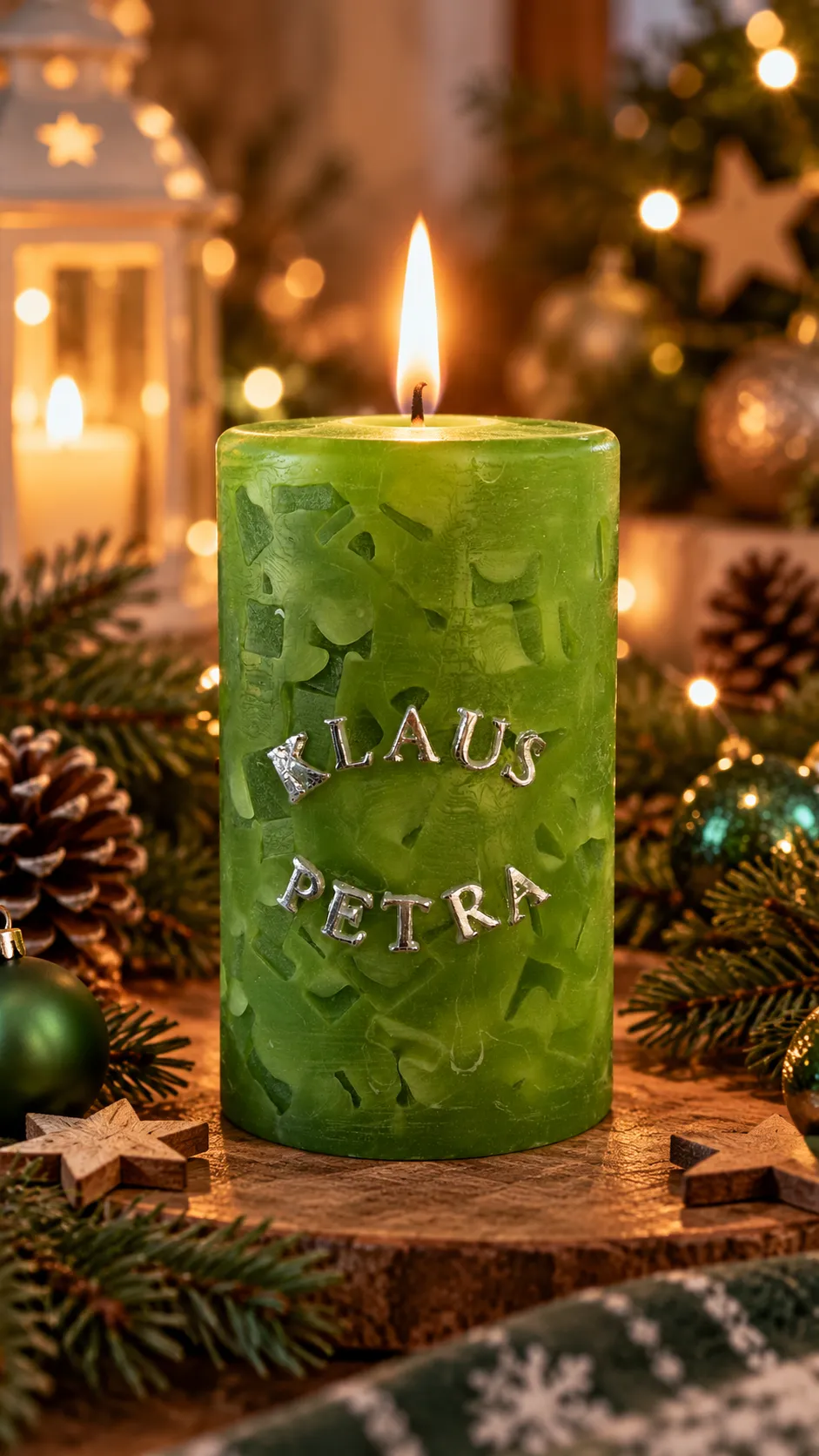 Brennende grüne Weihnachtskerze mit silbernen Buchstaben „KLAUS“ und „PETRA“ vor festlicher Weihnachtsdekoration.